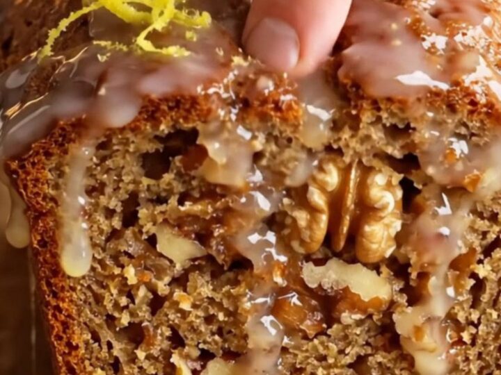 Sliced whole-lemon walnut loaf cake with a glossy white glaze and lemon zest curls on top