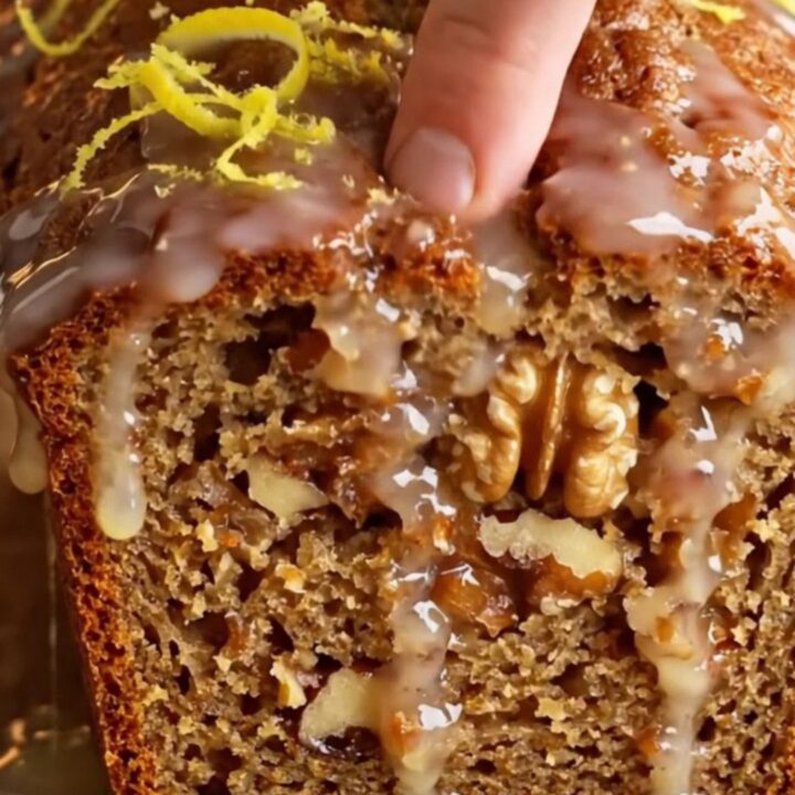 Sliced whole-lemon walnut loaf cake with a glossy white glaze and lemon zest curls on top