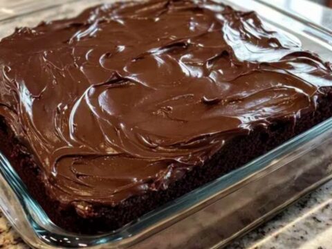 Gâteau au chocolat carré glacé d'un fondant brillant, dans un moule en verre posé sur un plan de travail en granit