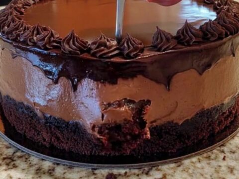 Gâteau mousse au chocolat entier sur un plan de travail, ganache brillante et rosettes pochetées en bordure