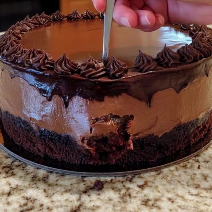 Gâteau mousse au chocolat entier sur un plan de travail, ganache brillante et rosettes pochetées en bordure