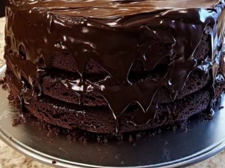 Gâteau au chocolat en trois couches sur un présentoir, ganache brillante coulant sur les bords