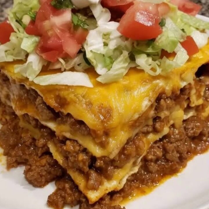 Tranche haute de lasagna de tacos sur assiette blanche, cheddar filant, laitue émincée