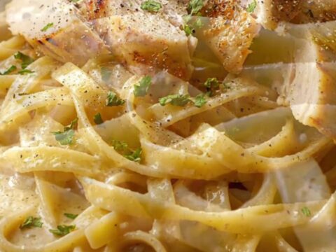 Creamy garlic parmesan chicken pasta in a skillet, with a fork twirling fettuccine and chicken slices on top.