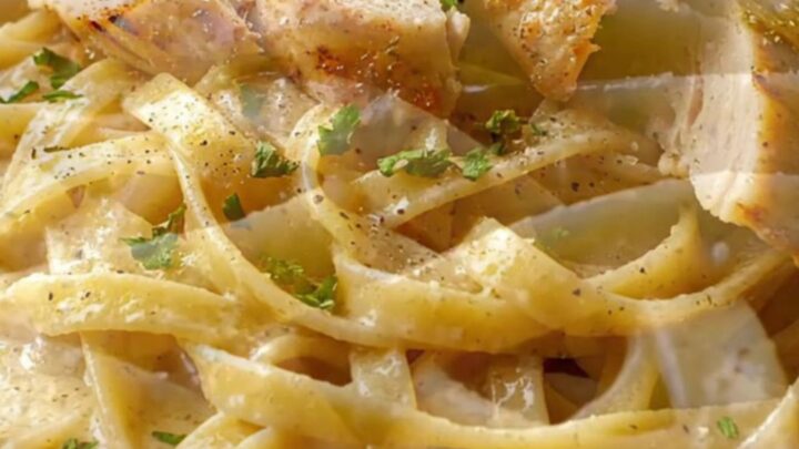 Creamy garlic parmesan chicken pasta in a skillet, with a fork twirling fettuccine and chicken slices on top.