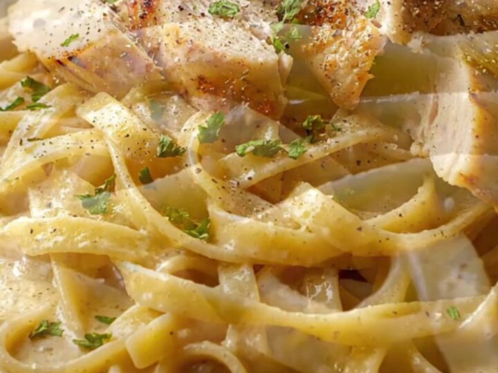 Creamy garlic parmesan chicken pasta in a skillet, with a fork twirling fettuccine and chicken slices on top.