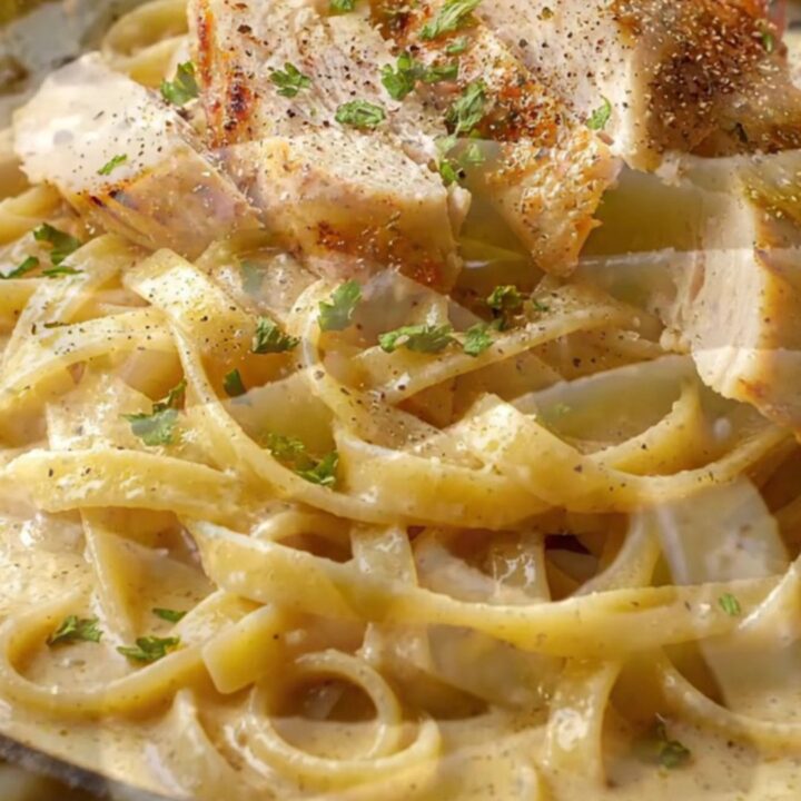Creamy garlic parmesan chicken pasta in a skillet, with a fork twirling fettuccine and chicken slices on top.
