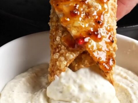 Crispy chicken shawarma wrap sliced in half, showing layers of chicken, fries, and sumac onions