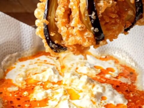 Golden crispy accordion eggplant fans on a platter with white garlic yogurt and red pepper butter