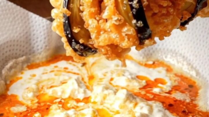 Golden crispy accordion eggplant fans on a platter with white garlic yogurt and red pepper butter