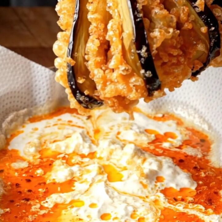 Golden crispy accordion eggplant fans on a platter with white garlic yogurt and red pepper butter