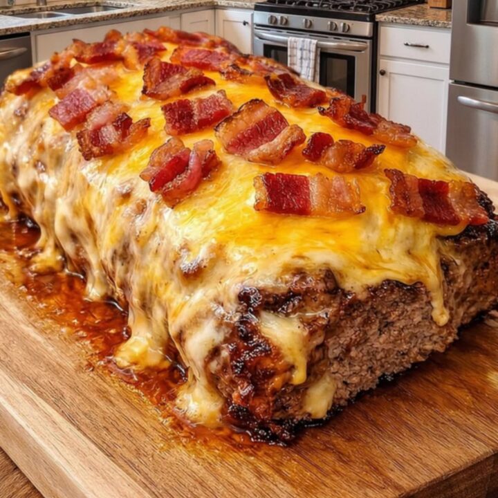A large, savory meatloaf resting on a wooden board, topped with melted cheddar cheese and crispy bacon bits.