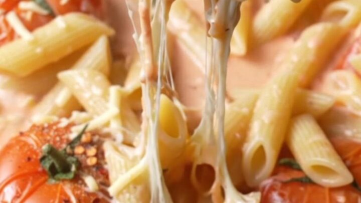 Creamy roasted tomato and garlic penne pasta in a skillet, with melted cheese stretching from a forkful