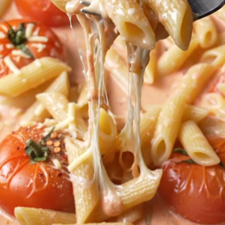 Creamy roasted tomato and garlic penne pasta in a skillet, with melted cheese stretching from a forkful
