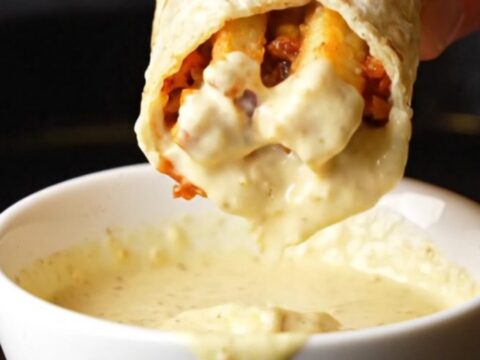A golden toasted chicken shawarma wrap cut in half, showing spiced chicken, fries, and garlic sauce oozing out.
