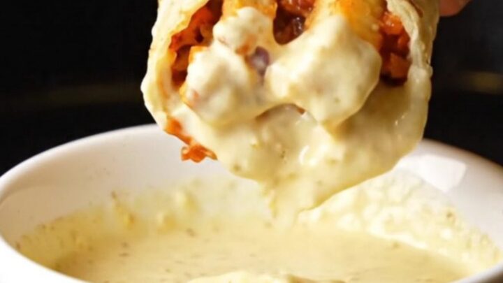 A golden toasted chicken shawarma wrap cut in half, showing spiced chicken, fries, and garlic sauce oozing out.