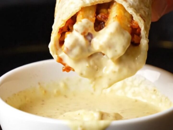 A golden toasted chicken shawarma wrap cut in half, showing spiced chicken, fries, and garlic sauce oozing out.