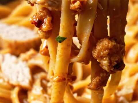 Creamy fettuccine Alfredo with chili crisp and sliced chicken breast, topped with parmesan flakes.