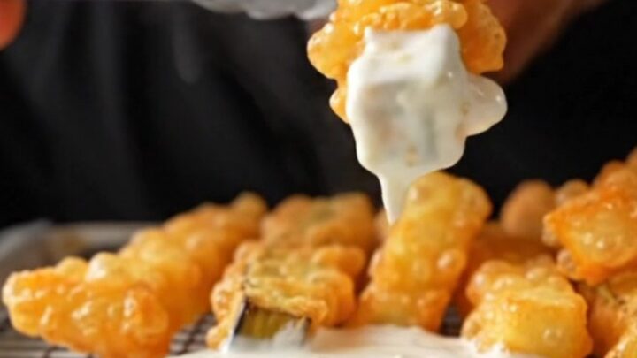 Golden crispy eggplant fries piled on a wire rack, with a bowl of garlic yogurt dip in the background