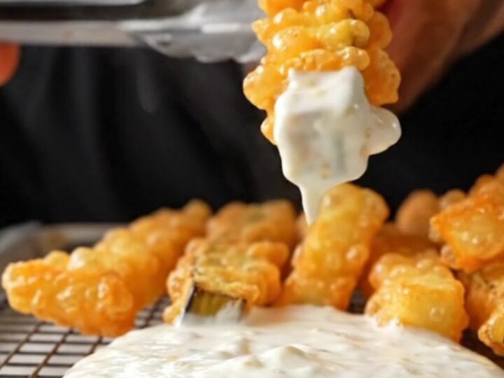 Golden crispy eggplant fries piled on a wire rack, with a bowl of garlic yogurt dip in the background