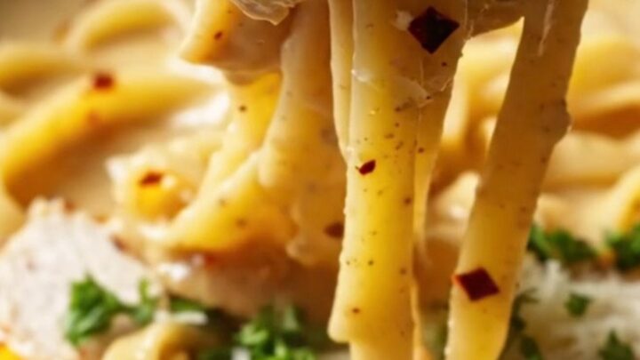 A fork twirling spicy chili crisp chicken Alfredo with creamy sauce and red chili flakes