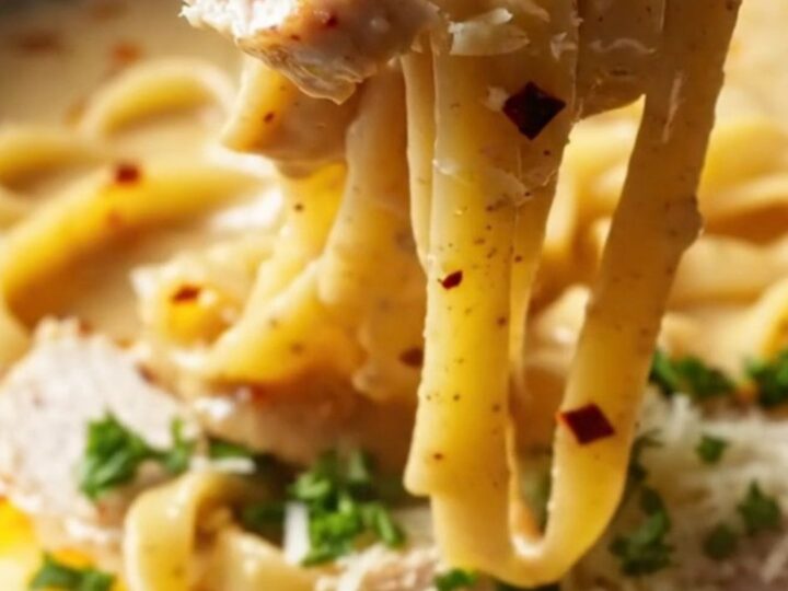 A fork twirling spicy chili crisp chicken Alfredo with creamy sauce and red chili flakes