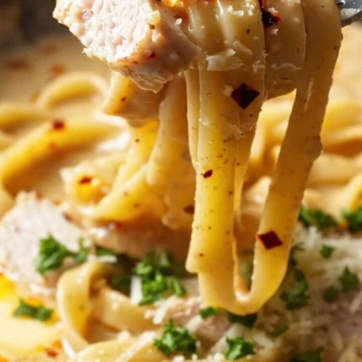 A fork twirling spicy chili crisp chicken Alfredo with creamy sauce and red chili flakes