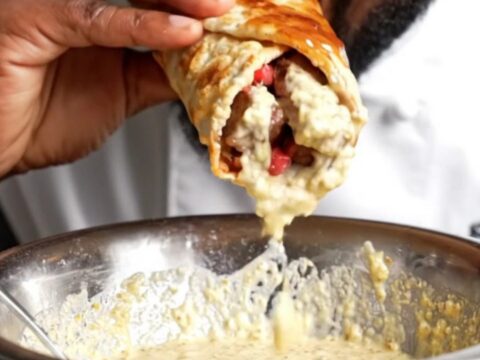 Crispy beef ribeye shawarma wrap with pomegranate glaze, cut in half showing juicy beef, fries, and onions