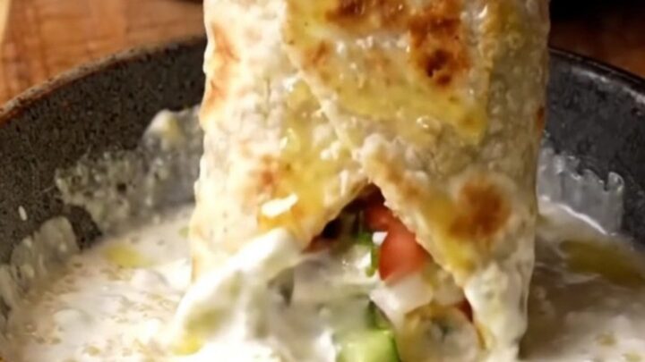 Crispy chicken shish wrap sliced diagonally, showing charred chicken, chopped salad, and garlic sauce.