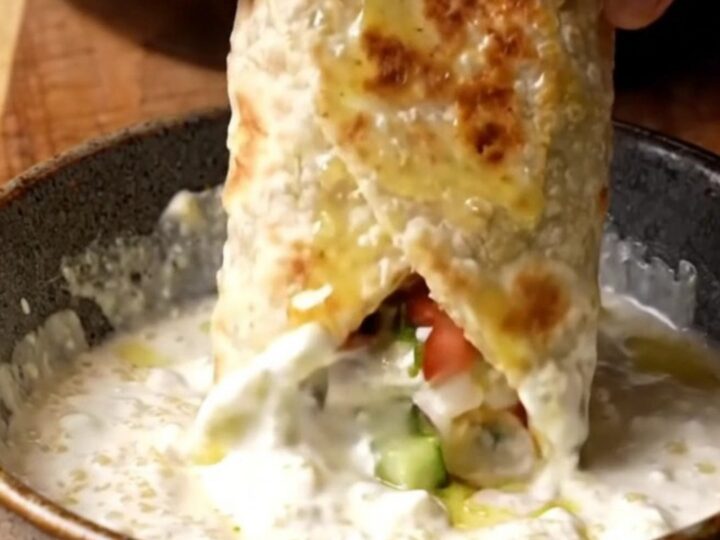 Crispy chicken shish wrap sliced diagonally, showing charred chicken, chopped salad, and garlic sauce.