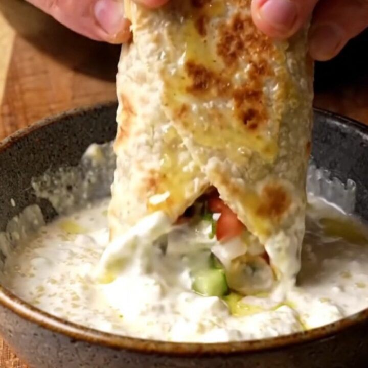 Crispy chicken shish wrap sliced diagonally, showing charred chicken, chopped salad, and garlic sauce.