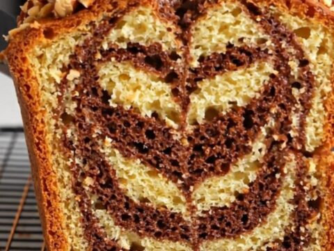 Sliced zebra marble hazelnut loaf cake showing chocolate and vanilla swirls, topped with roasted hazelnuts