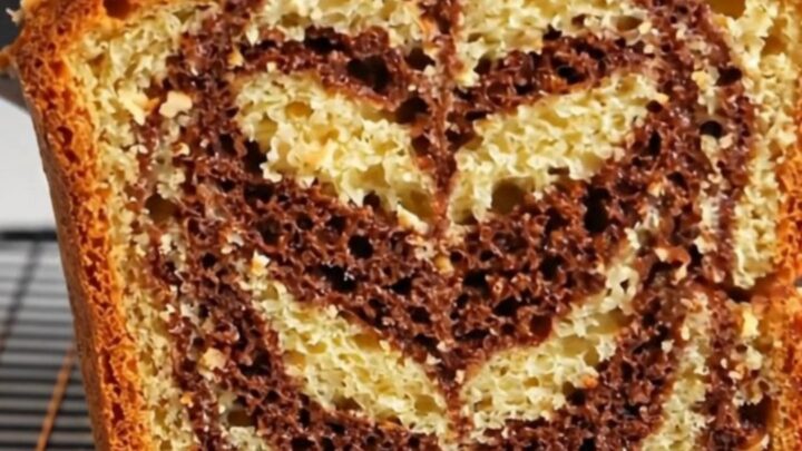 Sliced zebra marble hazelnut loaf cake showing chocolate and vanilla swirls, topped with roasted hazelnuts