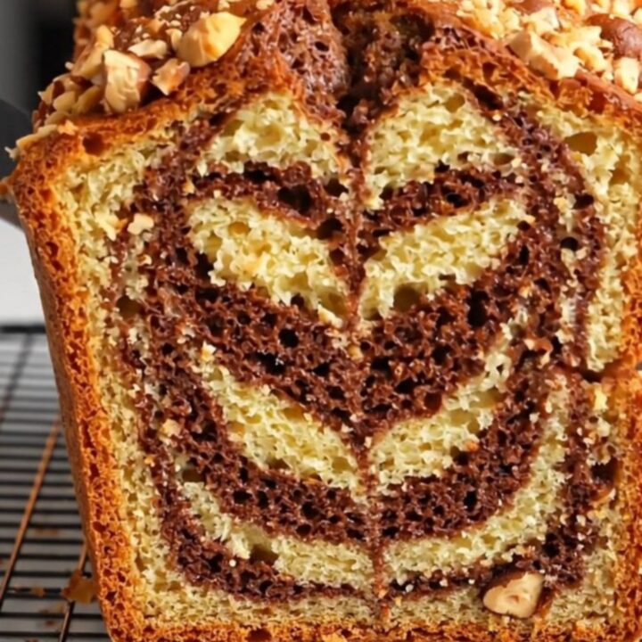 Sliced zebra marble hazelnut loaf cake showing chocolate and vanilla swirls, topped with roasted hazelnuts