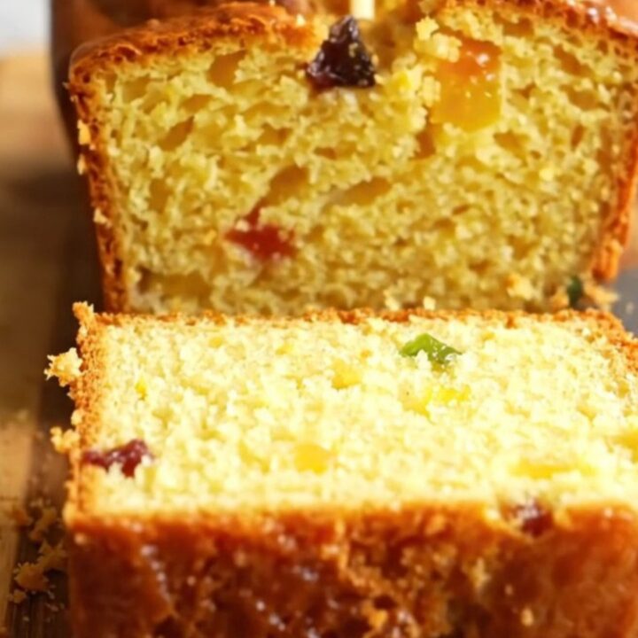 Sliced whole lemon loaf cake with visible dried fruits and a moist crumb