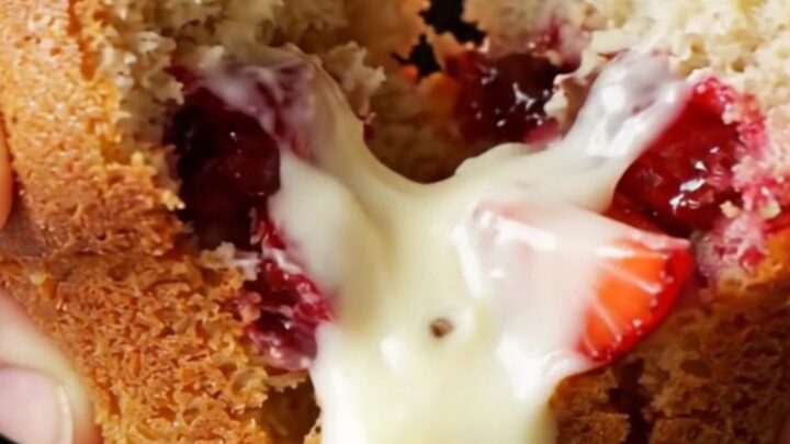 Golden bakery-style muffin split open showing melted white chocolate and strawberries
