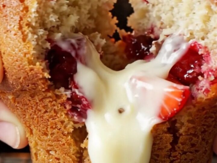 Golden bakery-style muffin split open showing melted white chocolate and strawberries