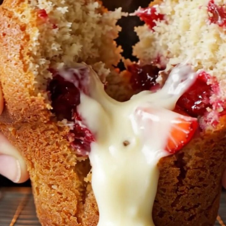 Golden bakery-style muffin split open showing melted white chocolate and strawberries