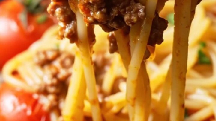 A fork twirling a glossy nest of spaghetti bolognese with blistered tomatoes and ground beef, garnished with parsley.