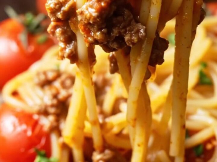 A fork twirling a glossy nest of spaghetti bolognese with blistered tomatoes and ground beef, garnished with parsley.