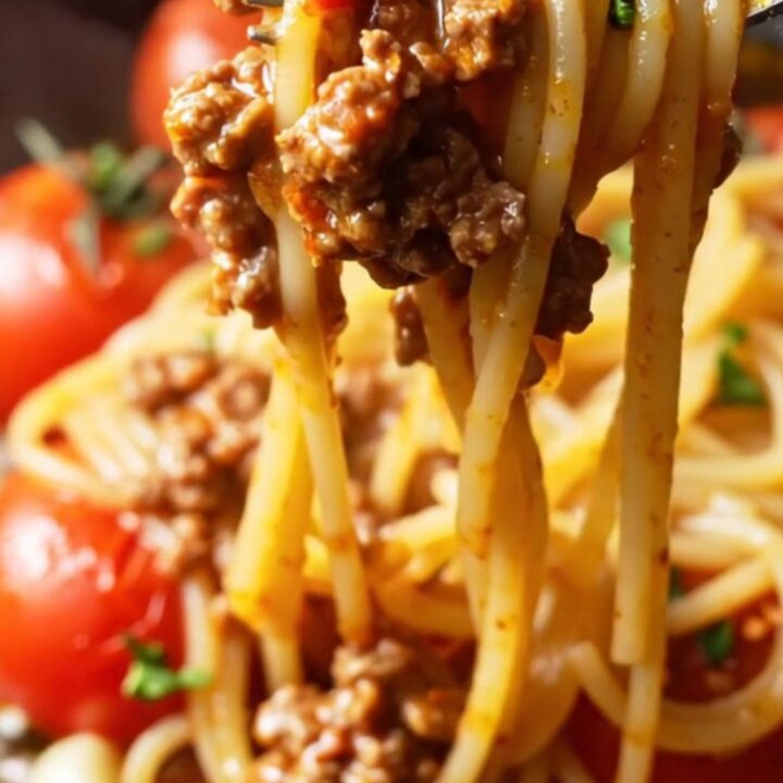 A fork twirling a glossy nest of spaghetti bolognese with blistered tomatoes and ground beef, garnished with parsley.
