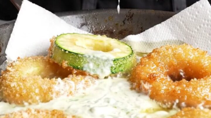 Golden crispy zucchini rings piled on a plate with a bowl of garlic yogurt dip