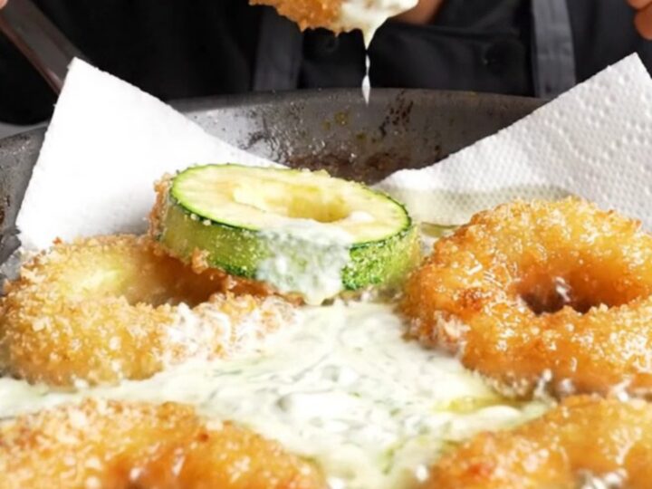 Golden crispy zucchini rings piled on a plate with a bowl of garlic yogurt dip