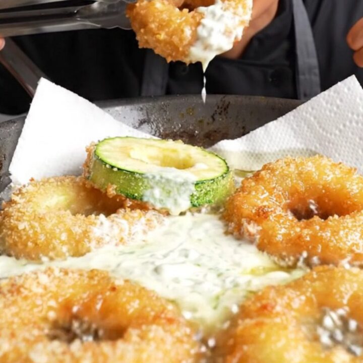 Golden crispy zucchini rings piled on a plate with a bowl of garlic yogurt dip