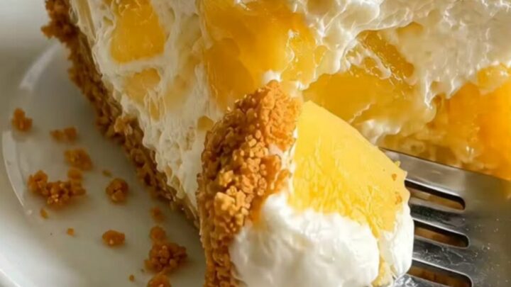A slice of no-bake pineapple cheesecake on a white plate with visible pineapple chunks and a golden graham crust.
