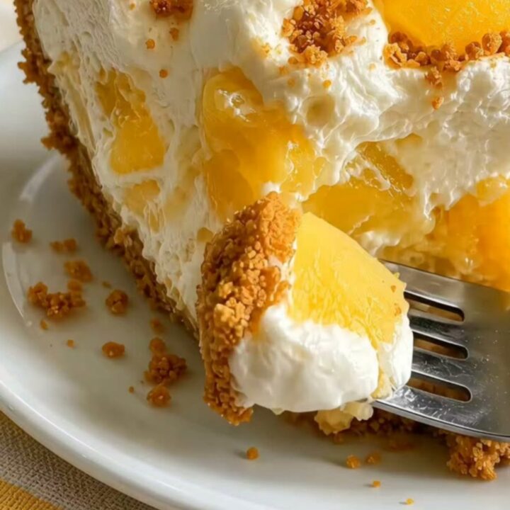 A slice of no-bake pineapple cheesecake on a white plate with visible pineapple chunks and a golden graham crust.