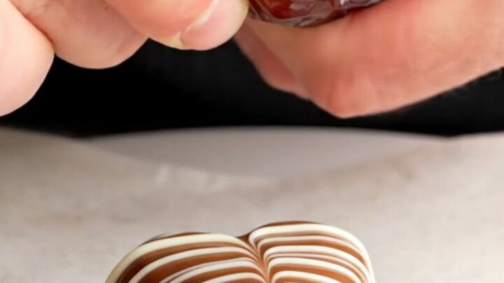 Chocolate-covered date hearts with marbled white chocolate pattern on a parchment-lined baking sheet
