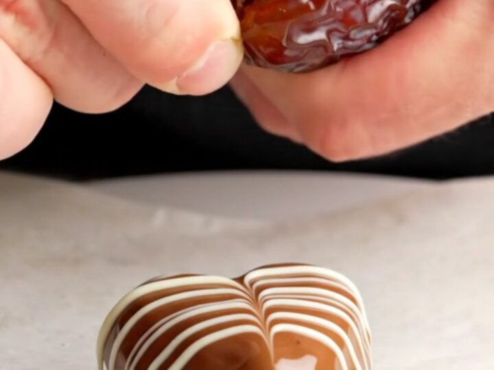 Chocolate-covered date hearts with marbled white chocolate pattern on a parchment-lined baking sheet