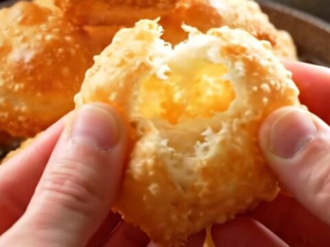 Golden Turkish fried dough pillows piled on a platter, with one torn open to show the airy interior