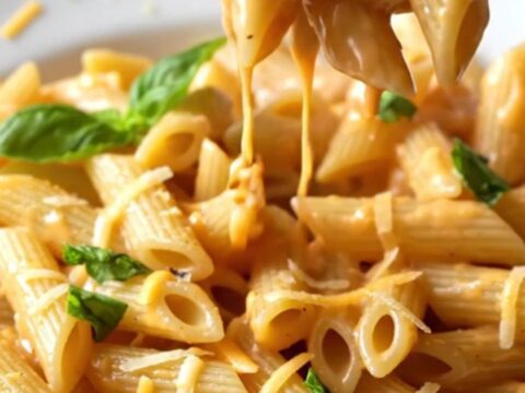 A fork lifting a creamy tomato penne pasta with melted cheese and fresh basil garnish